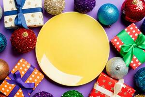 Top view of holiday setting on colorful background. Plate, gifts, baubles and Christmas decorations. New Year dinner concept photo