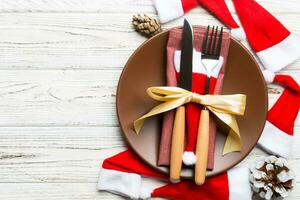 Holiday composition of plate and flatware decorated with Santa hat on wooden background. Top view of Christmas decorations with empty space for your design. Festive time concept photo