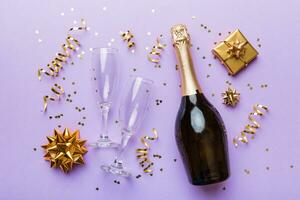 Bottle of champagne with colored glitter, confetti and gift box space for text on colorfull background, top view. Hilarious, christmas and birthday celebration photo