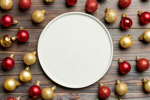 Top view of festive plate with red and golden baubles on wooden background. Christmas decorations and toys. New Year advent concept photo