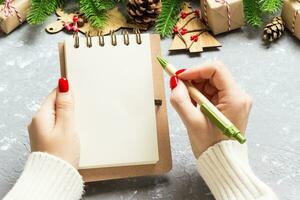 Top view of female hand writing in a notebook on cement Christmas background. fir tree and festive decorations. Wish list. New Year concept photo