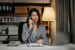 Young beautiful woman work late from home in room at late night overtime.Businesswoman bending over workplace while looking at laptop computer. photo