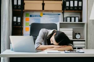 asiático mujer sensación migraña cabeza tensión.con exceso de trabajo mujer de negocios financiero mientras trabajando en ordenador portátil y tableta foto