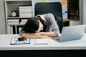 asiático mujer sensación migraña cabeza tensión.con exceso de trabajo mujer de negocios financiero mientras trabajando en ordenador portátil y tableta foto