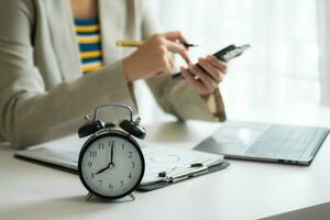 Alarm clock on the desk. Business hand using smartphone, laptop and tablet  working in modern office building photo