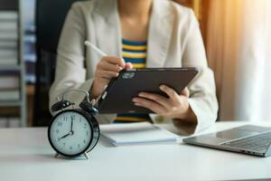 Alarm clock on the desk. Business hand using smartphone, laptop and tablet  working in modern office building photo
