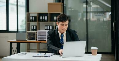 Young business man working at office with laptop, tablet and taking notes on the paper. photo