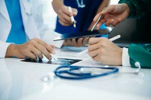 Medical team having a meeting with doctors in white lab coats and surgical scrubs seated at a table discussing a patients working online using computers photo