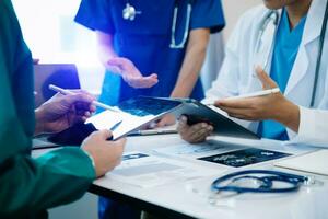 Medical team having a meeting with doctors in white lab coats and surgical scrubs seated at a table discussing a patients working online using computers photo