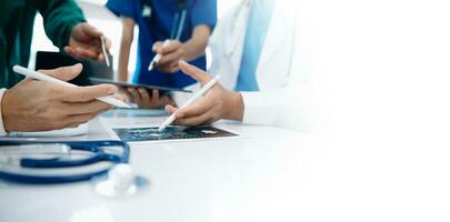 Medical team having a meeting with doctors in white lab coats and surgical scrubs seated at a table discussing a patients working online using computers photo