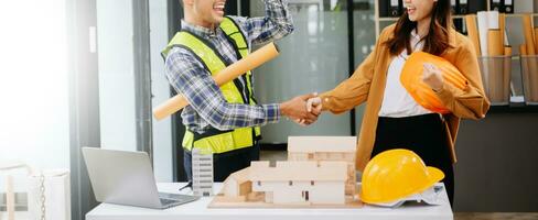 Construction team shake hands greeting start new project plan behind yellow helmet on desk in office center to consults about their building project. photo