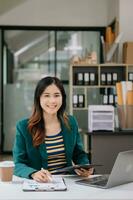 Confident business expert attractive smiling young woman typing laptop ang holding digital tablet on desk in office. photo