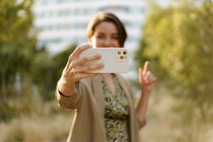 Happy woman using mobyle phone while walking in autumn park. Wearing stylish green jacket and dress.  Lifetstyle portrait. photo