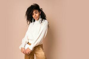 Sensual african american woman  looking at camera. Studio shot of beautiful black female model isolated on beige background.Wearing silk pants and elegant sweater. photo