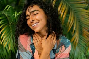 Outdoor  portrait of blissful  lovely woman with curly hairs posing over tropical trees and palm leaves. photo