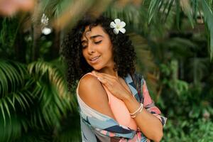 Close up portrait of  blissful woman with  plumeria flower in hairs after spa in   luxury resort. Wearing boho tropical outfit. photo