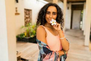 feliz mujer con tropical flor en mano posando en lujo spa hotel. spa y cuerpo cuidado concepto. foto