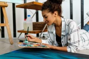 Woman painter lies on the floor  near  canvas and drawing. Artist studio interior. Drawing supplies, oil paints, artist brushes, canvas, frame.  Creative concept. photo