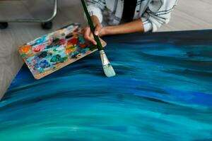 Artist Woman  drawing ocean waves on canvas.  Work in process. Top view.  Holding brush and palette. Oil paint. photo