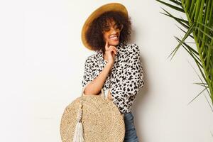 Happy  mix race  female in trendy blouse and straw hat  standing over white wall. Perfect white  smile. Shopping mood. photo