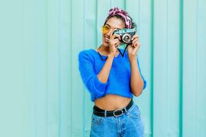 Outdoor lifestyle  image of fashionable  black woman in bright wool sweater and colorful  headband on hairs making photos by film camera.