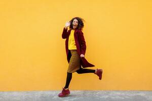 Full length image of excited black woman jumping with happy face expression on yellow background. photo