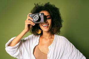 cerca arriba retrato de afican mujer participación retro Cámara fotográfica y riendo terminado verde antecedentes en estudio. foto