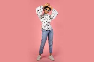 Fashionable african woman in white blouse and jeans posing on pink background. photo