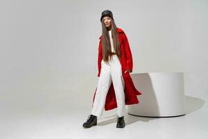 Fashion studio photo of stylish european brunette woman in red coat and black hat posing on white background.  Trendy winter accsesorises. Full lenght.