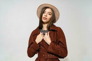 cerca arriba interior estudio Moda retrato de maravilloso mujer en elegante invierno marrón Saco y negro sombrero posando en blanco antecedentes. foto