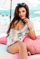 Summer portrait of beautiful brunette woman chilling  in the beach club. Tropical acsessories. photo
