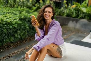 woman chilling on bench   and using mobyle phone. Wearing  purple blouse and stylish sneakers. Modern  environment. photo