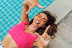 Close up top view portrait of  cute playful  woman in stylish sunglasses  chilling near swimming pool. Summer season, vacation and travel concept. photo