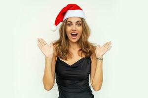 Pretty woman with suprice face in santa hat and relegant black dress  posing on white background in studio. photo