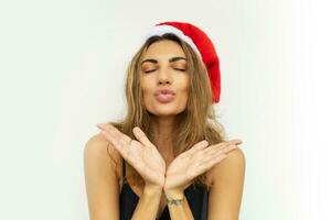 Happy woman in santa hat and sexy black party dress send kiss to camera. Posing on white background. photo