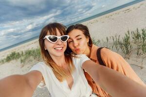 two women smiling and posing for the camera on the beach photo