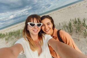 two women smiling and posing for the camera on the beach photo