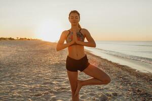 a woman in a sports bra and shorts is doing yoga on the beach photo