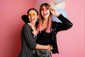 Two women , best friends  celebrating hen party, posing with bridal photo props on pink background.