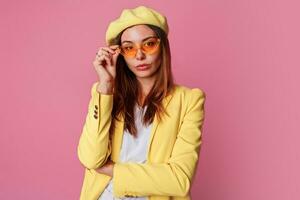 agraciado elegante mujer en brillante amarillo ropa en pie terminado rosado antecedentes. altura Moda mirar. foto