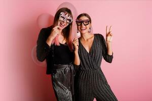 Two women , best friends  celebrating hen party, posing with bridal photo props on pink background.