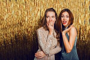 Close up studio image of two amazing sexy celebrating girls  with red lips, surprise face, laughing , posing on golden sparkly background. New year party mood. photo