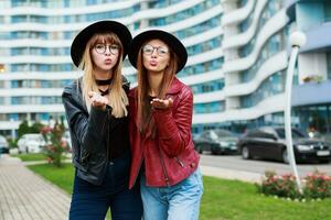 Couple of two stylish woman in trendy spring outfit sending air-kiss to camera .  Wearing leather jacket. Round glasses. Autumn fashion look. photo