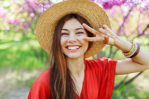 Playful cute girl making funny face and showing signs , posing in spring park on blooming trees background. photo