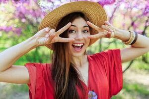 Playful cute girl making funny face and showing signs , posing in spring park on blooming trees background. photo