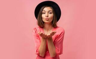 Lovely brunette short haired woman sen kiss to camera and posing on pink background. photo