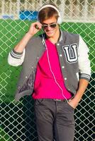 Outdoor fashion portrait of handsome guy in stylish  spring sportive outfit, listening favorite music  and posing near sports field. Bright contrast colors. photo