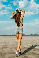 Beautiful slim tanned fitness girl 's back  with  hands on top. Posing outdoor in stylish jeans shorts. Soft light. photo