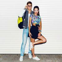 Fashion image of  stylish young  couple in love , tourists , posing near white urban wall. Wearing cool spring clothes, vintage camera,  bright neon back pack , sneakers. photo