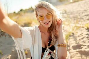 Close up portrait of smiling woman with blonde hairs making self portrait on sunny evening beach. photo